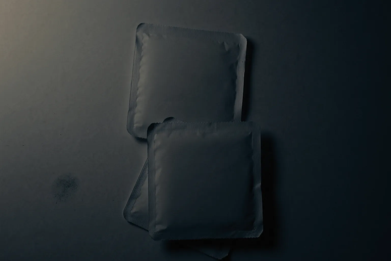 Sachets de préservatifs, sans marque ni impression, sur un plan sombre.
